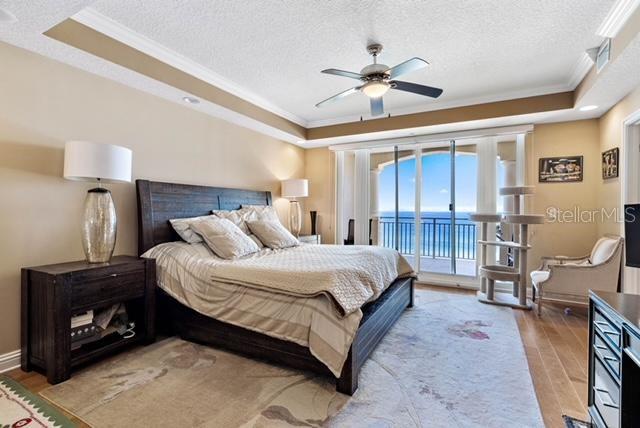 bedroom featuring access to outside, light wood-type flooring, a textured ceiling, ceiling fan, and a raised ceiling