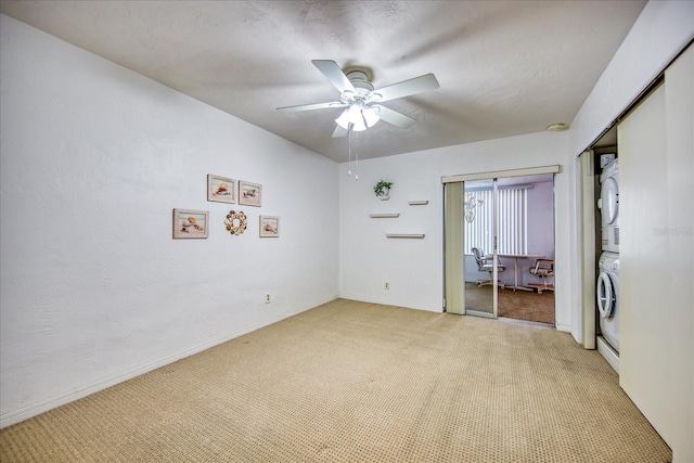 carpeted empty room with stacked washer / drying machine and ceiling fan