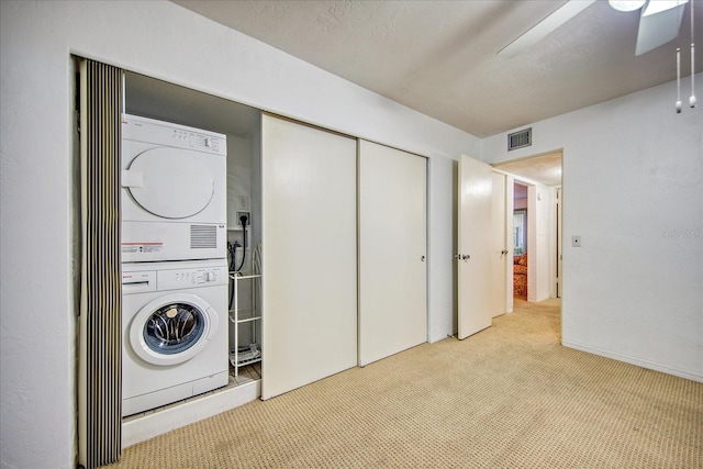 clothes washing area featuring light carpet, ceiling fan, and stacked washer and clothes dryer