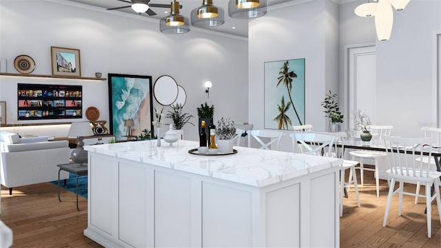 kitchen with ornamental molding, pendant lighting, white cabinets, light stone counters, and light hardwood / wood-style floors