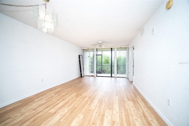 empty room with ceiling fan with notable chandelier, a wall of windows, light wood-type flooring, and a textured ceiling