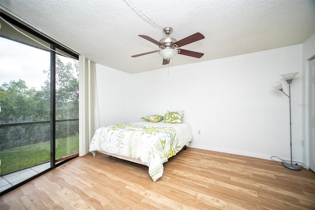 bedroom featuring wood-type flooring, ceiling fan, a wall of windows, and a textured ceiling