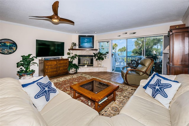 living room featuring hardwood / wood-style floors, a high end fireplace, ceiling fan, ornamental molding, and a textured ceiling