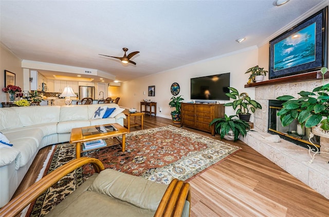 living room featuring hardwood / wood-style flooring, ceiling fan, a stone fireplace, and ornamental molding