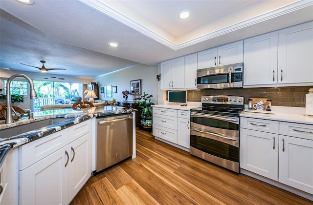 kitchen with white cabinetry, ceiling fan, backsplash, appliances with stainless steel finishes, and light wood-type flooring