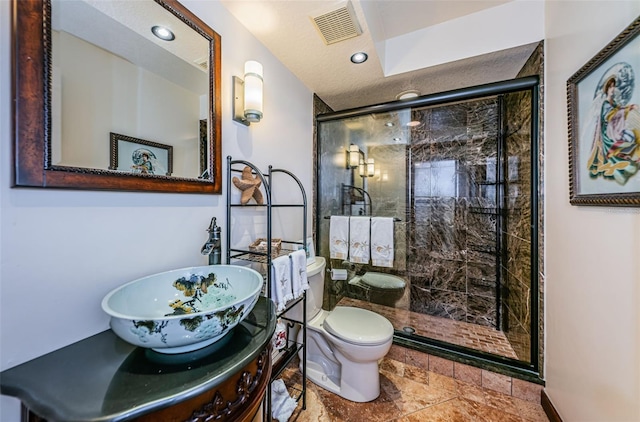 bathroom featuring vanity, toilet, a shower with shower door, and a textured ceiling