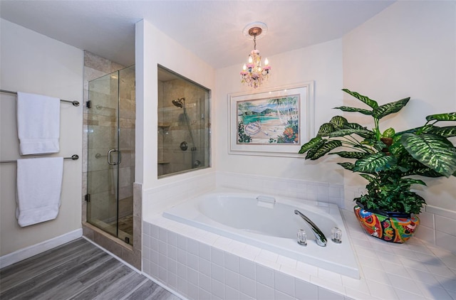 full bath featuring a garden tub, an inviting chandelier, a stall shower, wood finished floors, and baseboards