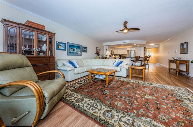 living room with ceiling fan, ornamental molding, wood finished floors, and baseboards