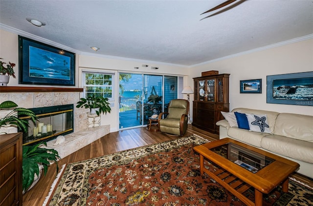 living room with a textured ceiling, a stone fireplace, crown molding, and wood finished floors