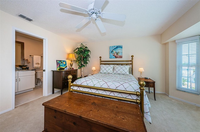 bedroom featuring light carpet, baseboards, visible vents, connected bathroom, and a textured ceiling