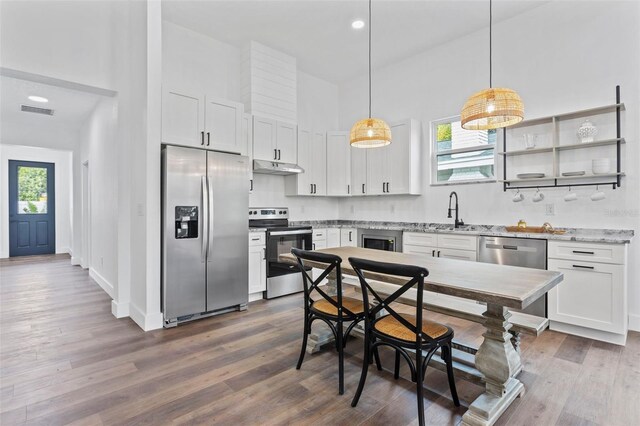 kitchen with appliances with stainless steel finishes, white cabinets, wood-type flooring, and hanging light fixtures