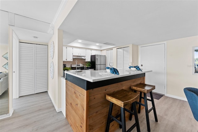 kitchen with appliances with stainless steel finishes, light wood-type flooring, a breakfast bar, a raised ceiling, and white cabinetry