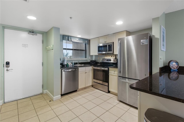 kitchen with light tile patterned floors, appliances with stainless steel finishes, dark stone countertops, and sink