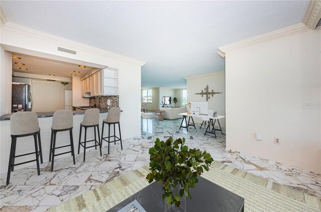 kitchen with crown molding, stainless steel refrigerator, backsplash, a kitchen bar, and light brown cabinets