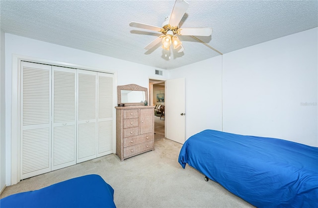 bedroom with a closet, a textured ceiling, light colored carpet, and ceiling fan