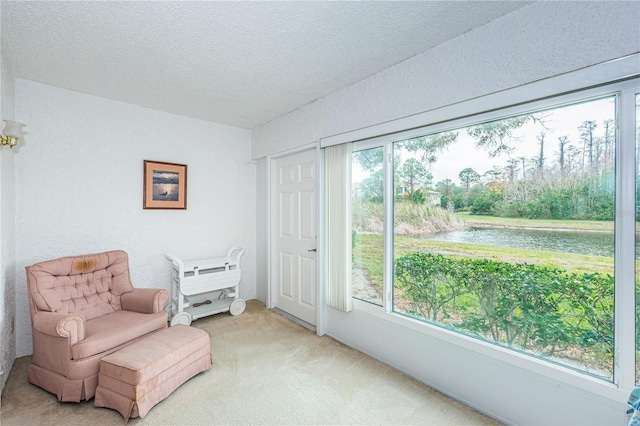 sitting room with light carpet, a water view, and a textured ceiling