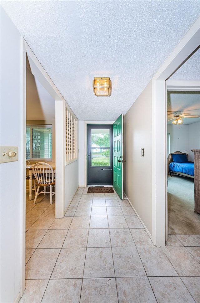 doorway to outside featuring light tile flooring, ceiling fan, and a textured ceiling