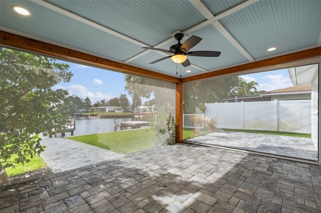 view of patio with a water view, fence, a boat dock, and ceiling fan