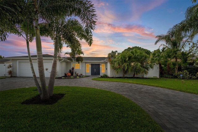 view of front facade with decorative driveway, a yard, stucco siding, an attached garage, and fence