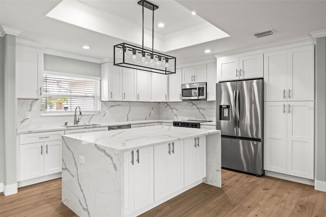 kitchen with a raised ceiling, a kitchen island, stainless steel appliances, white cabinetry, and a sink