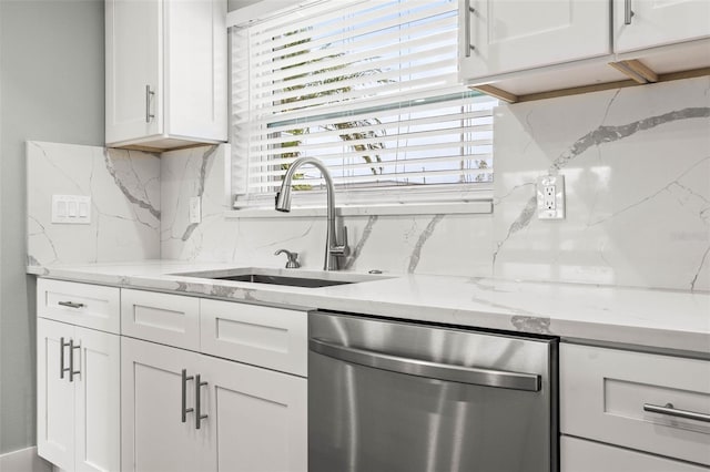 kitchen with light stone counters, white cabinetry, dishwasher, and a sink