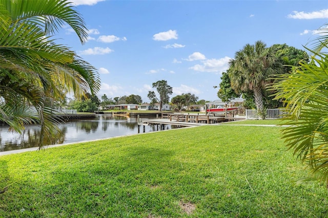 dock area featuring a water view, a lawn, and fence