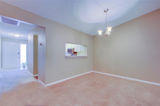 carpeted spare room with a textured ceiling, vaulted ceiling, and a chandelier