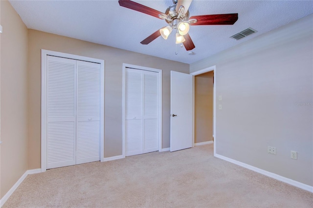 unfurnished bedroom featuring ceiling fan, a textured ceiling, light carpet, and two closets