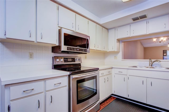 kitchen with appliances with stainless steel finishes, sink, white cabinets, backsplash, and an inviting chandelier