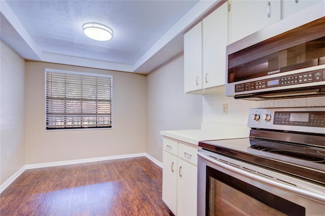 kitchen featuring appliances with stainless steel finishes, white cabinetry, a tray ceiling, dark hardwood / wood-style flooring, and decorative backsplash