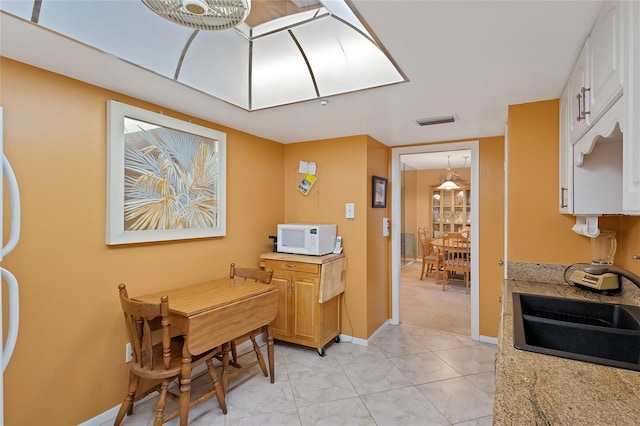 kitchen with sink, white cabinets, light tile floors, and light stone counters