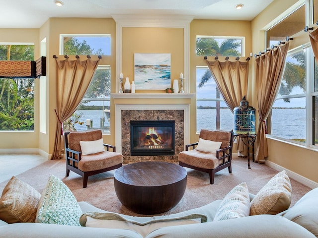 sitting room featuring a high end fireplace, a wealth of natural light, light carpet, and a water view