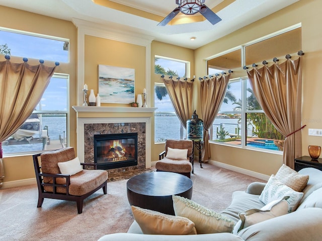 sitting room with a raised ceiling, a fireplace, ceiling fan, light carpet, and a water view