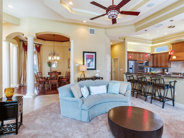 living room with ornate columns, a towering ceiling, a raised ceiling, ceiling fan with notable chandelier, and crown molding