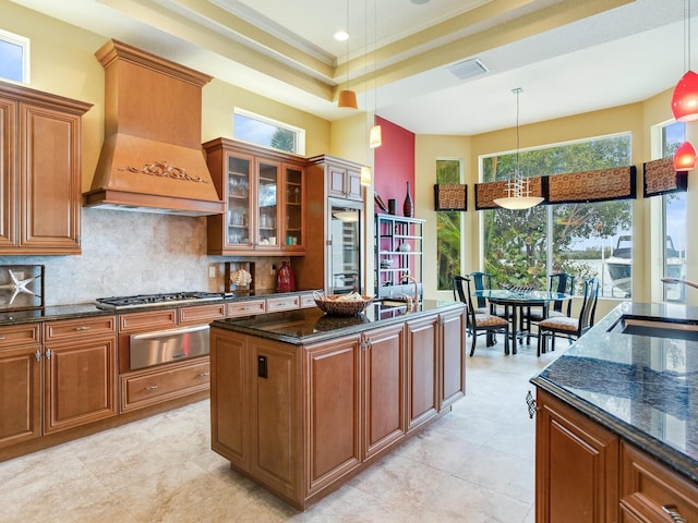 kitchen featuring custom exhaust hood, stainless steel appliances, crown molding, dark stone counters, and pendant lighting