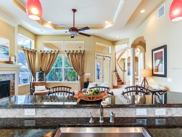 kitchen with a high end fireplace, a raised ceiling, ornamental molding, and dark stone countertops