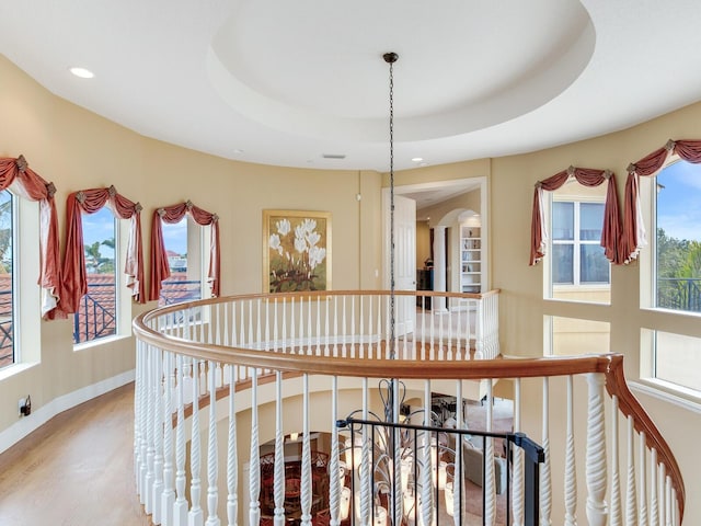 hall featuring hardwood / wood-style floors, a raised ceiling, and a chandelier