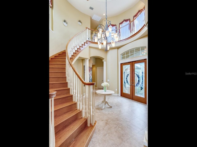 foyer entrance featuring french doors, a towering ceiling, a chandelier, and ornate columns