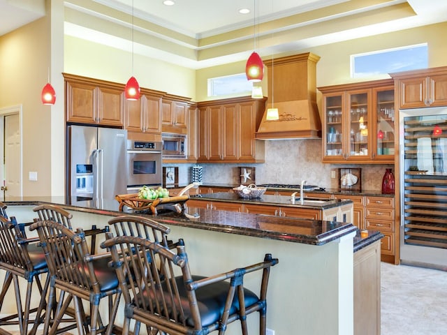 kitchen with stainless steel appliances, custom range hood, a kitchen bar, dark stone counters, and crown molding