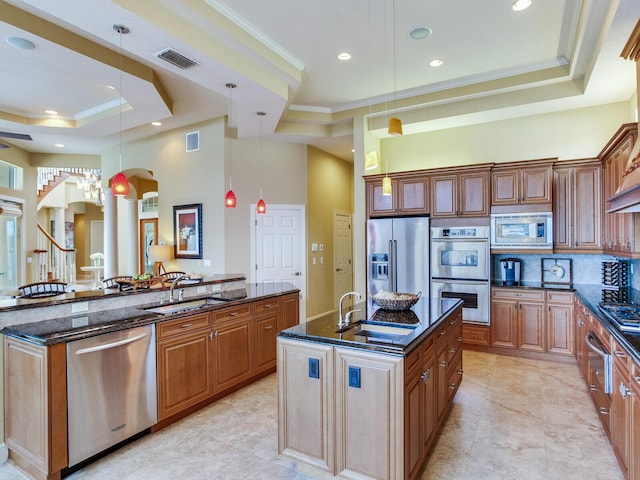 kitchen with decorative light fixtures, an island with sink, a tray ceiling, appliances with stainless steel finishes, and sink