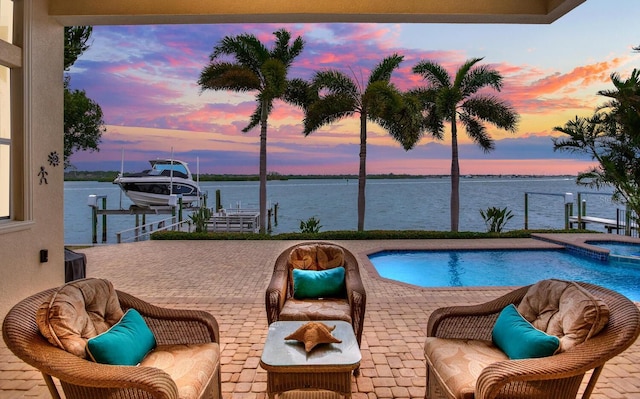 pool at dusk featuring a patio area, a dock, and a water view