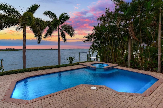 pool at dusk featuring a patio area, an in ground hot tub, and a water view