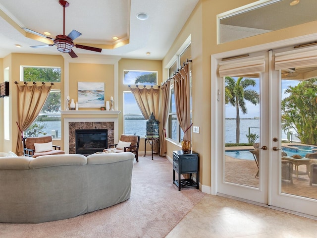 carpeted living room featuring a water view, french doors, a raised ceiling, ceiling fan, and ornamental molding