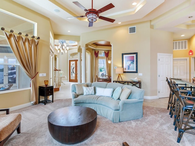 living room featuring ornate columns, ceiling fan, a tray ceiling, ornamental molding, and light carpet