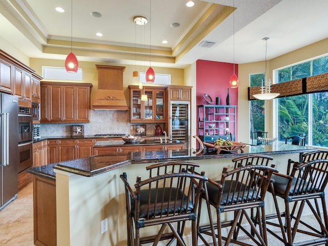 kitchen with ornamental molding, a kitchen bar, a raised ceiling, and custom range hood