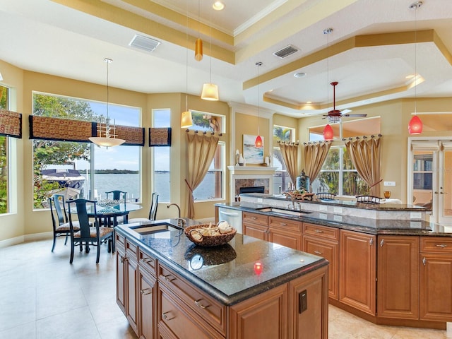 kitchen with a water view, pendant lighting, a center island with sink, a tray ceiling, and crown molding