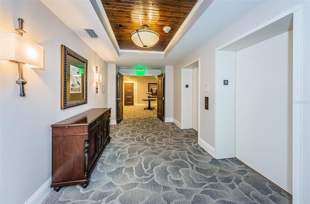 hall featuring wood ceiling, elevator, dark carpet, and a tray ceiling