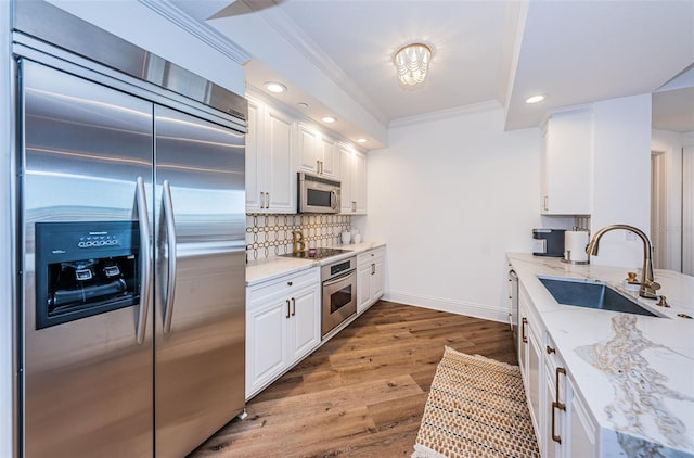 kitchen with light stone countertops, hardwood / wood-style floors, appliances with stainless steel finishes, white cabinets, and sink