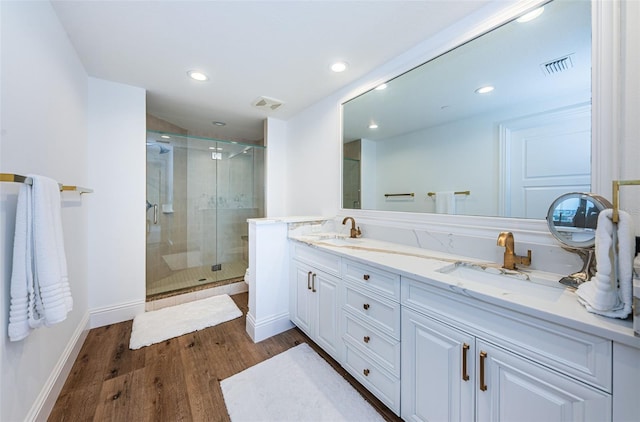 bathroom with vanity with extensive cabinet space, dual sinks, a shower with shower door, and hardwood / wood-style flooring