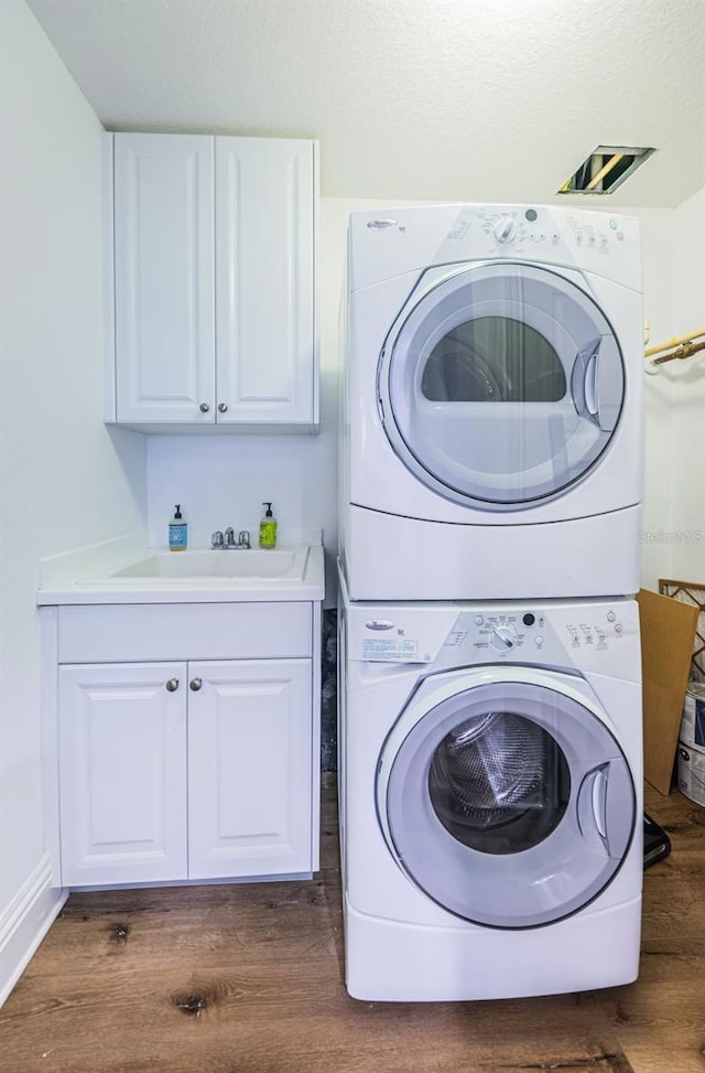 laundry area featuring stacked washer / dryer, cabinets, sink, and dark hardwood / wood-style flooring